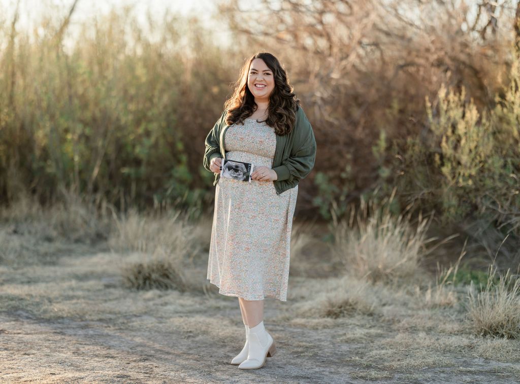 Maternity photographer in Midland TX. Mom holding sonogram image in an outdoor portrait.